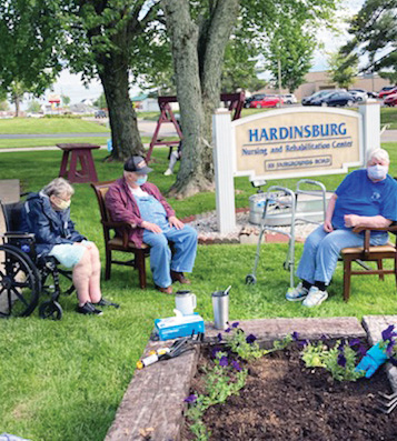 three hardinsburg nursing and rehab residents sitting outside next to the flower garden