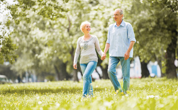older couple holding hands walking through the park on a sunny day
