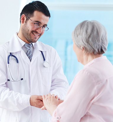 Young male doctor smiling and holding older adult woman's hand