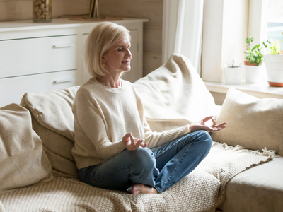 woman in cream sweater, meditating on couch