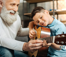 older man with white beard, teaching grandson how to play guitar