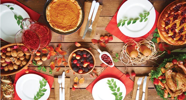 top view of a table set for Thanksgiving with turkey, pies, fruits, and nuts along with fall foliage.