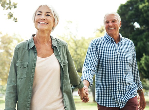 Older adult couple, woman and man walking hand-in-hand in the park.